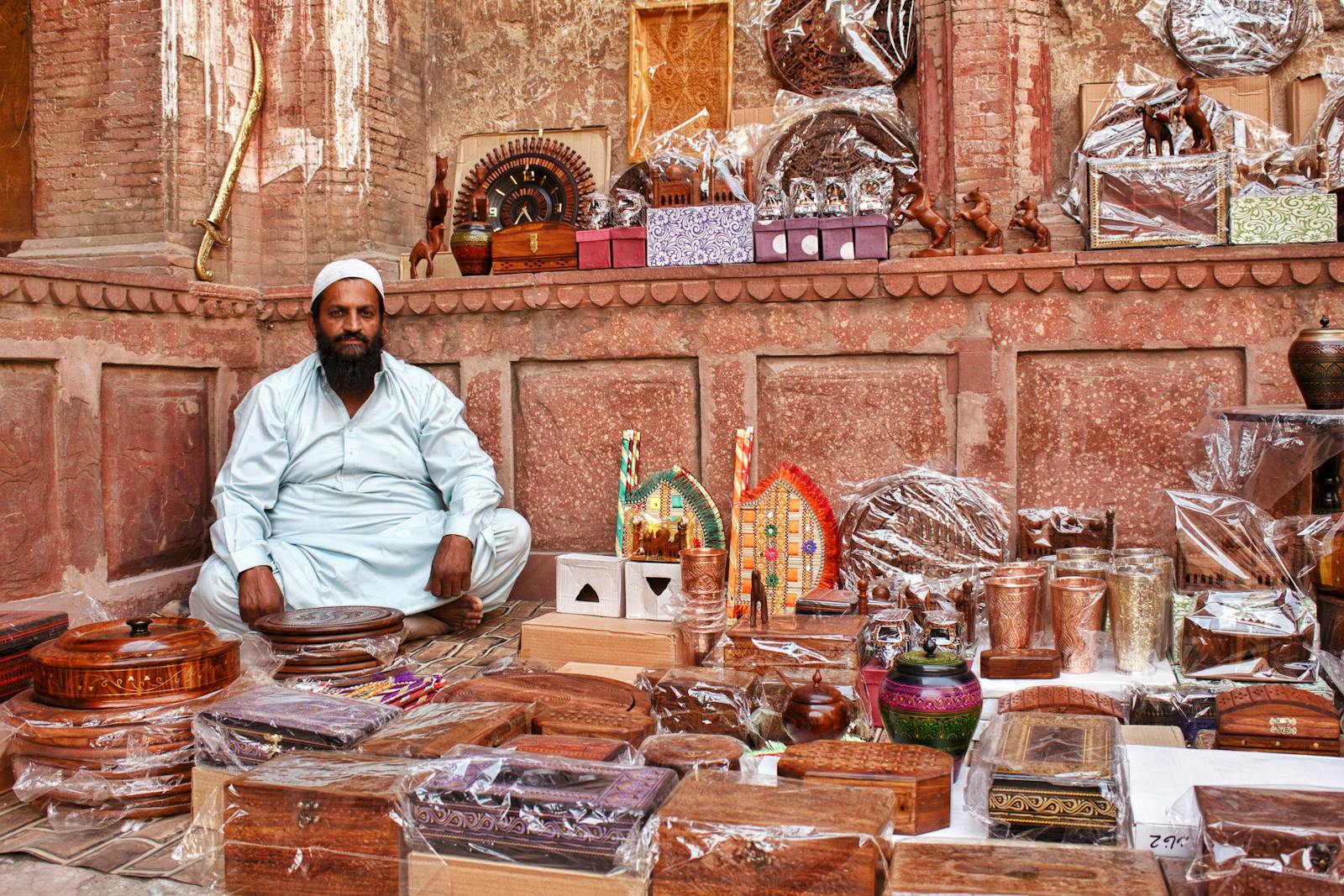 Vendor at Lahore bazaar surrounded by traditional Pakistani handicrafts and ornaments.