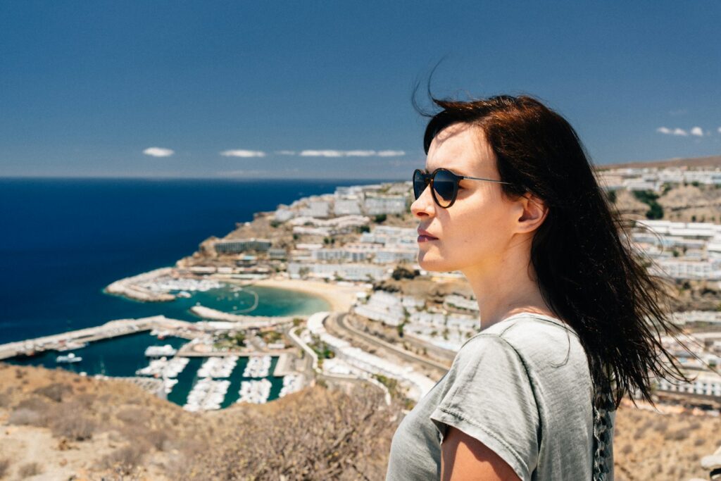 woman in grey t-shirt standing on top of hill overlooking city and sea