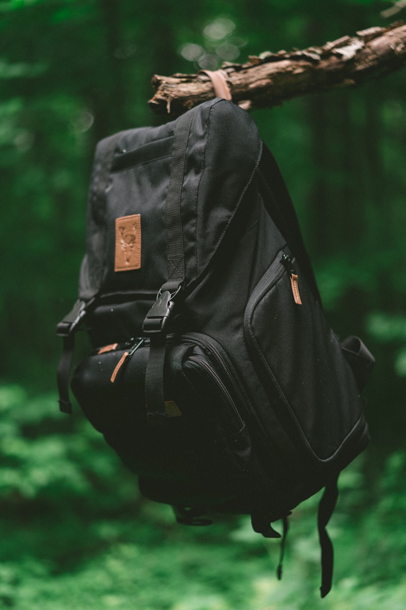 selective focus photo of black backpack hanging on brown tree branch